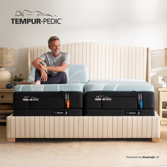 Man sitting on a Tempur-Pedic mattress in a bedroom setting with the brand logo above.