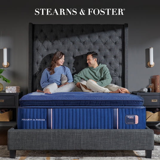 Stearns & Foster mattress with a couple sitting on it in a bedroom setting.