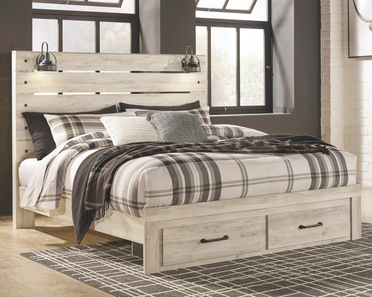 A light whitewashed wood platform bed frame with built-in storage drawers at the foot, styled with plaid and textured bedding in a rustic bedroom setting.