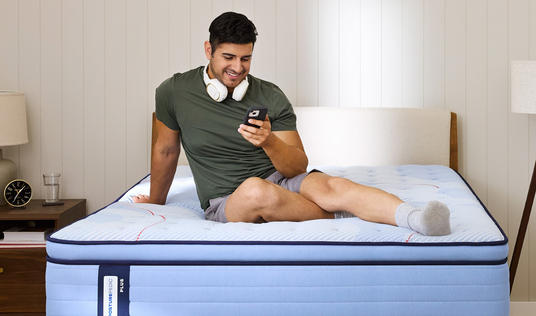 Man sitting on a mattress using a smartphone in a bedroom setting