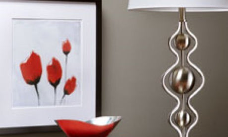 A red bowl in front of a red painting next to a silver lamp