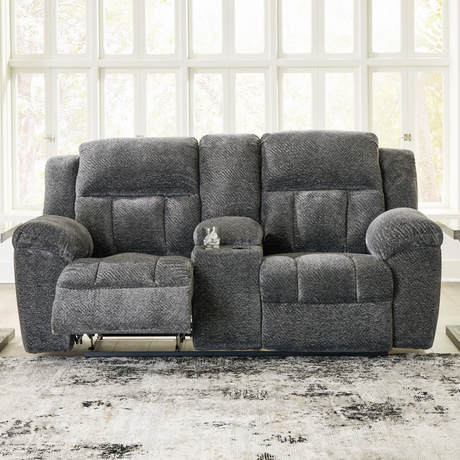 Gray reclining sofa in a living room setting with large windows.