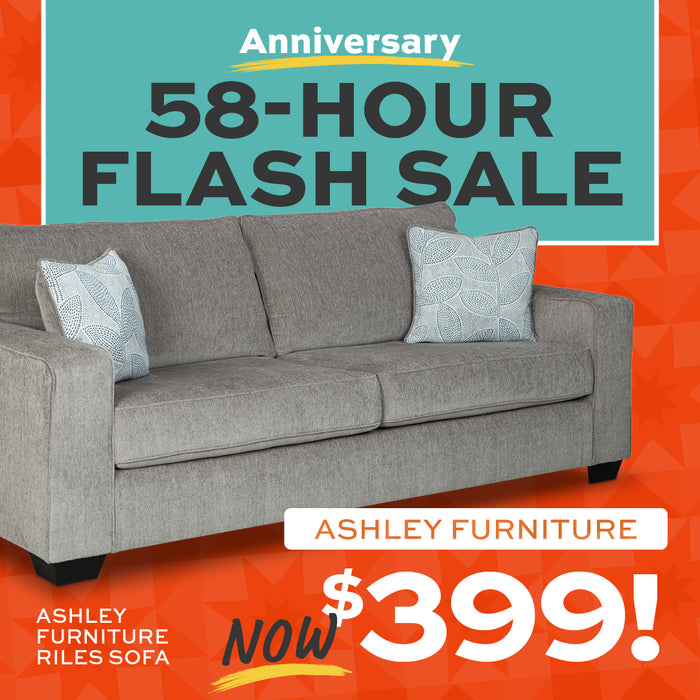 Gray sofa with decorative pillows on a red and blue background, promoting an Ashley Furniture sale.