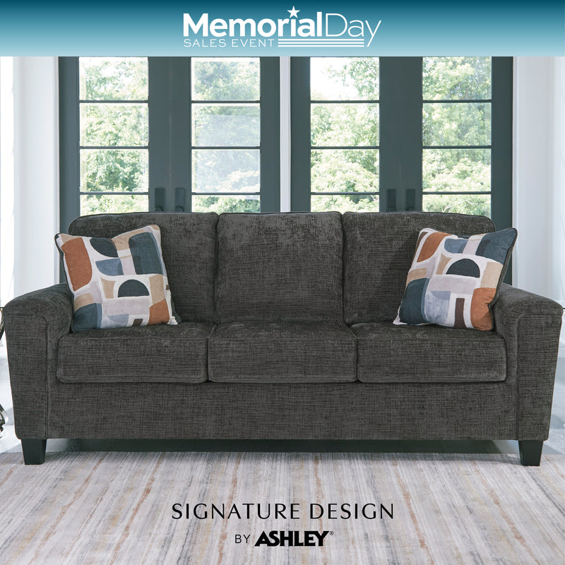 Gray sofa with patterned pillows in a room with large windows, featuring Memorial Day sales text and Signature Design by Ashley branding.
