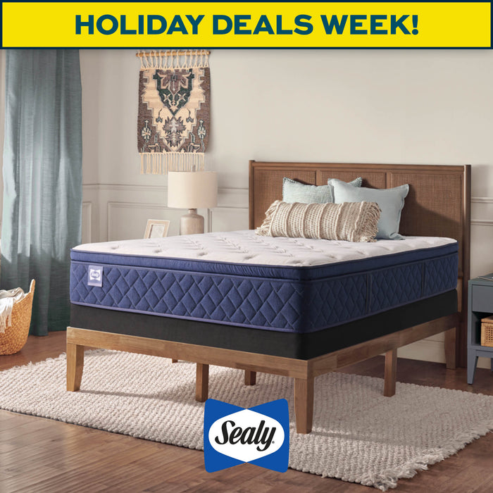 Blue mattress on a wooden bed frame with 'Sealy' logo and 'Holiday Deals Week!' text in a bedroom setting.