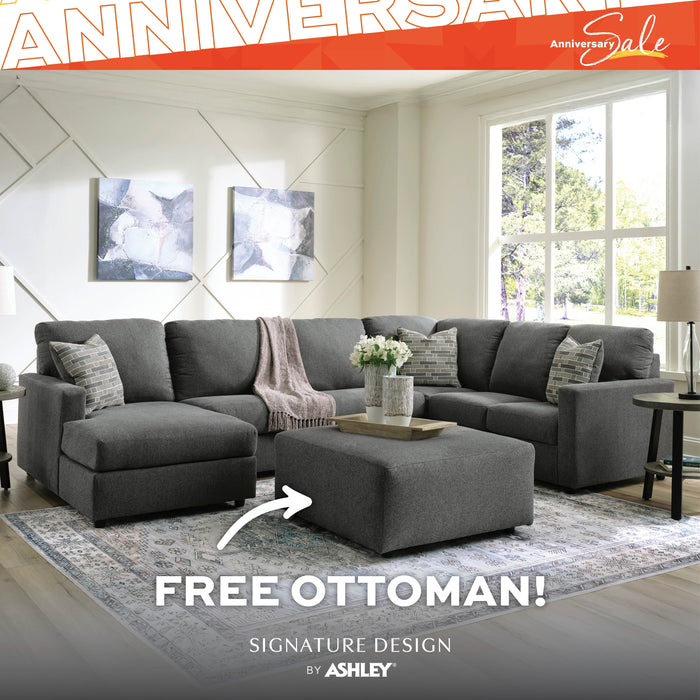 Gray sectional sofa with free ottoman in a living room setting, featuring Ashley Furniture branding.