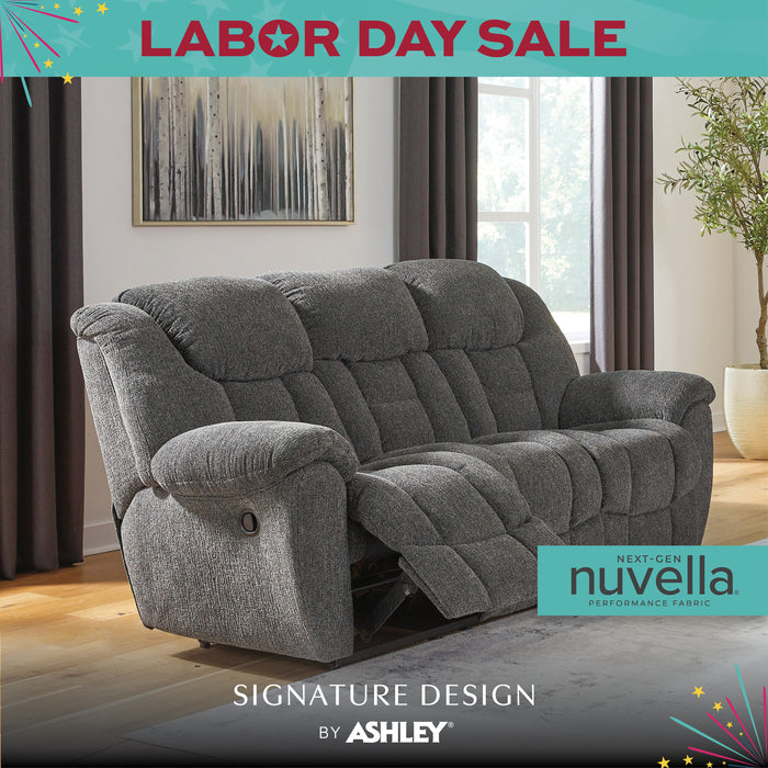Gray recliner sofa in a living room setting with 'Labor Day Sale' and 'Signature Design by Ashley' text.