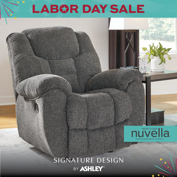 Gray recliner chair in a living room setting with 'Labor Day Sale' text and Ashley Furniture logo.