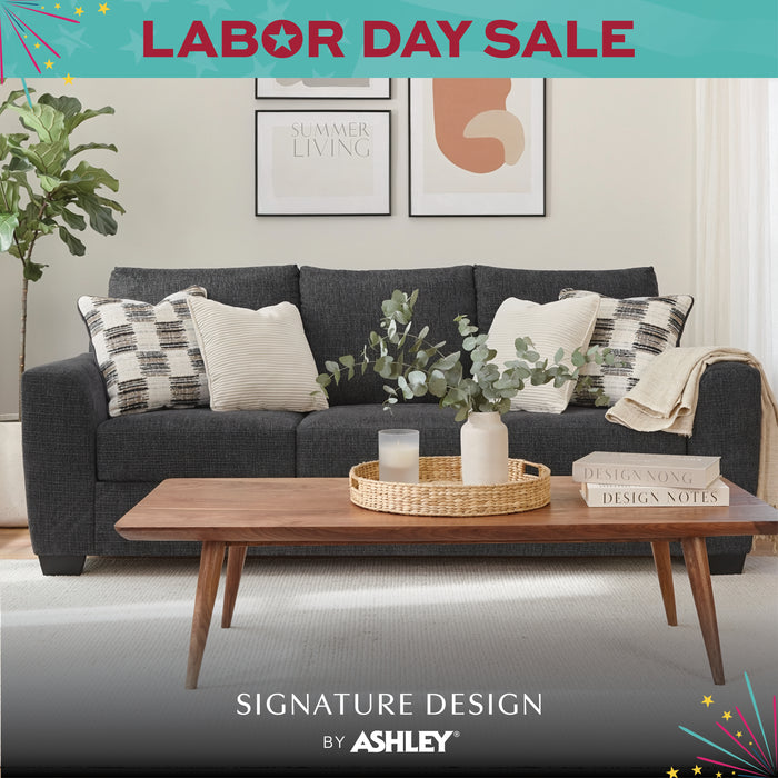 Living room with a gray sofa, wooden coffee table, and decorative elements. 'Labor Day Sale' and 'Signature Design by Ashley' text is present.