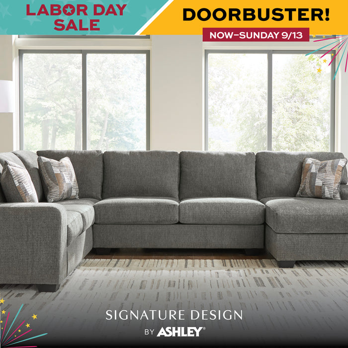 A large gray sectional sofa with a left chaise and patterned accent pillows, shown in a bright living room with large windows. Promotional sale banners appear at the top and bottom with the text 'Labor Day Sale,' 'Doorbuster!,' and 'Signature Design by Ashley.