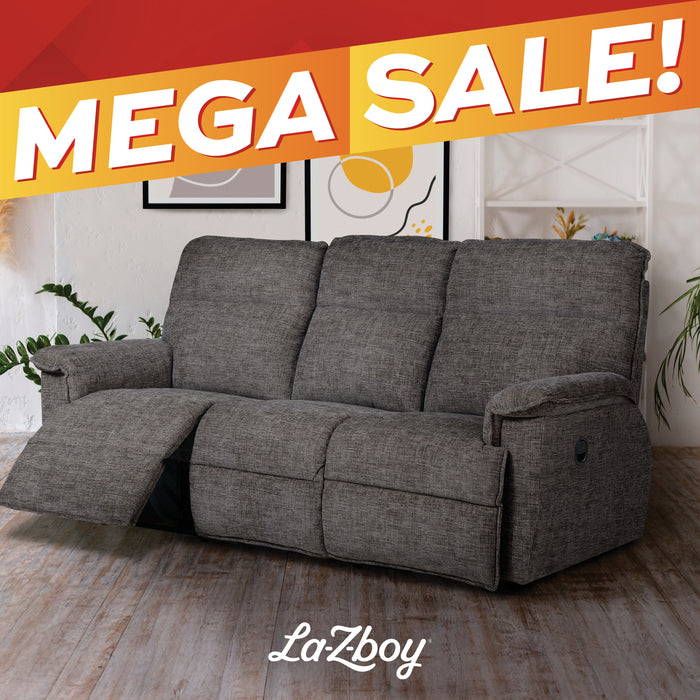 A gray upholstered reclining loveseat sofa shown in a staged living room setting with a wood floor, wall art, shelving, and plants. A large orange and red 'MEGA SALE!' banner overlays the top of the image, and the brand name 'LaZboy' appears at the bottom.