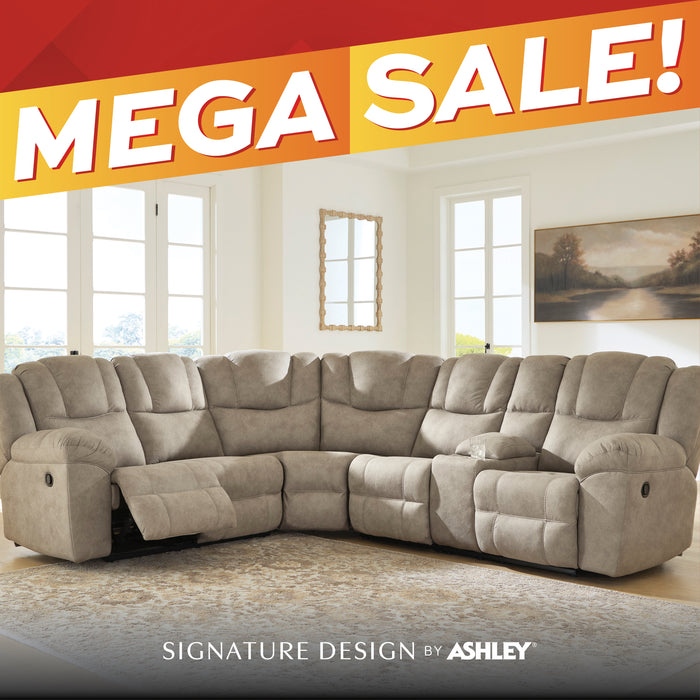 A large beige upholstered sectional recliner sofa shown in a bright living room, with a red and orange 'MEGA SALE!' banner across the top and 'SIGNATURE DESIGN BY ASHLEY' text at the bottom.