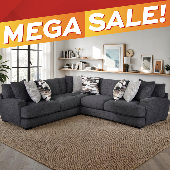 A dark gray fabric sectional sofa with patterned throw pillows, shown in a styled living room setting with a large woven rug, wall shelves, and a window. A bold orange and red 'MEGA SALE!' banner overlays the top of the image.