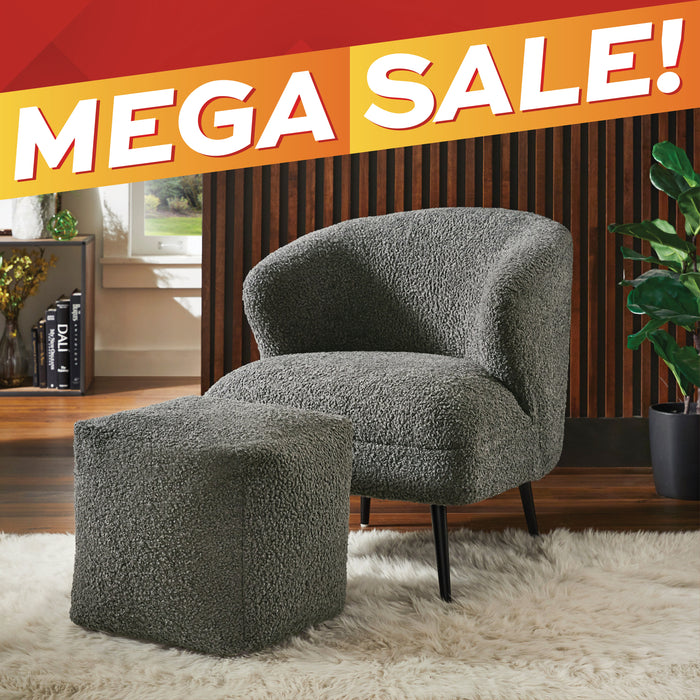 A gray bouclé armchair with a matching ottoman in a styled room setting, featuring a wood slat wall, white shag rug, potted plant, and a red and orange 'MEGA SALE!' banner across the top.