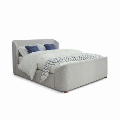 A modern upholstered bed with a textured light gray fabric, styled with white bedding, two blue accent pillows, and a blue-and-white patterned throw blanket, set against a plain white background.
