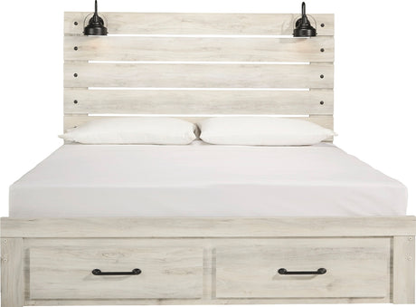 A light whitewashed wood bed frame with a slatted headboard, two built-in black wall-mounted lamps, white bedding, and two storage drawers with black handles at the bottom.