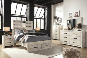 A rustic light gray wood bedroom furniture set including a bed with a slatted headboard, two matching nightstands, a dresser, and a tall chest of drawers, styled in a modern loft-style room with black walls and large windows.