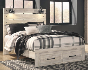 A rustic light gray wood platform bed frame with built-in storage drawers at the foot and a matching headboard, styled with black and white plaid bedding, pillows, and a dark throw blanket in a bedroom setting.