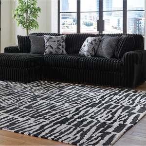 Black sofa with patterned cushions on a black and white patterned rug in a room with large windows.