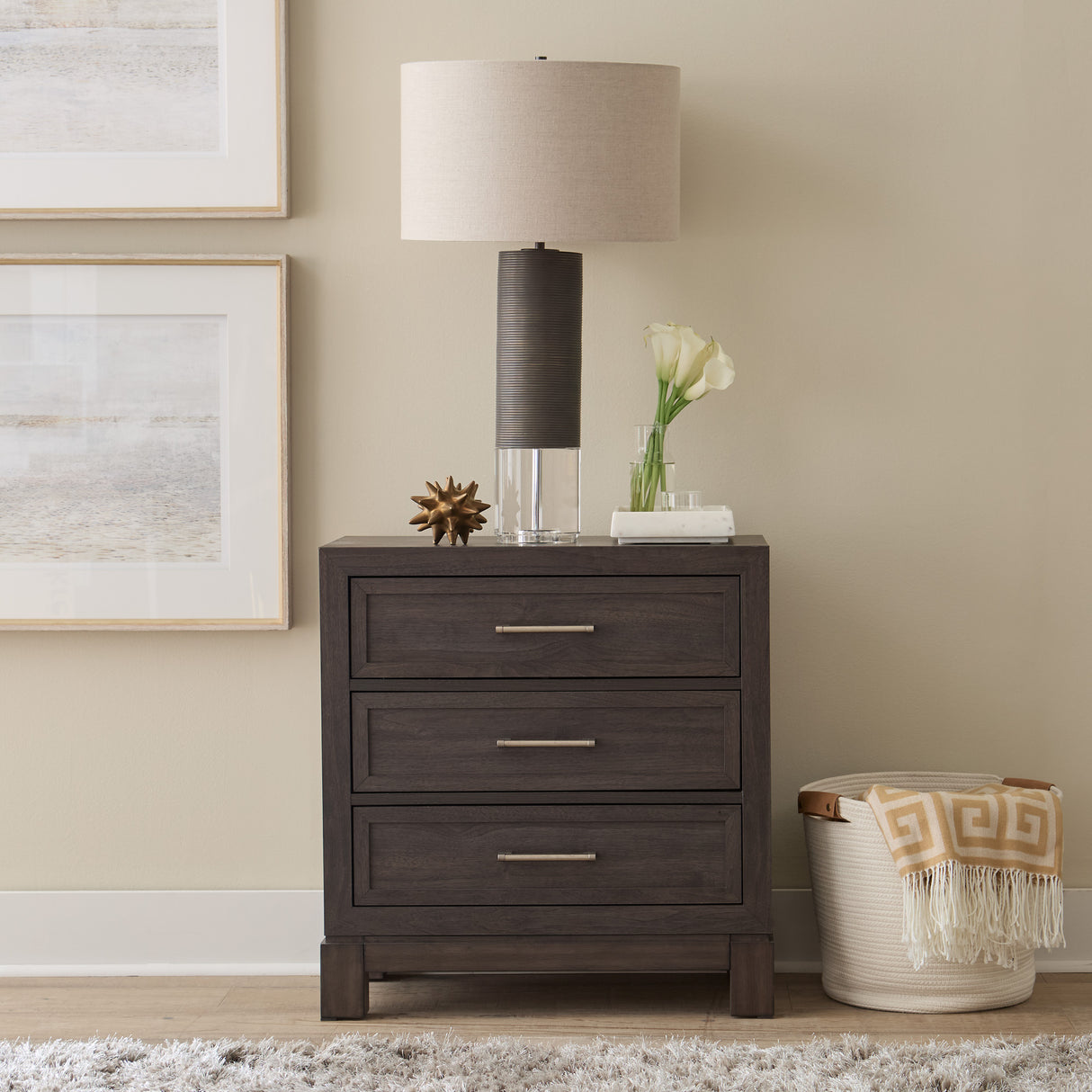 Dark wood nightstand with lamp, decor items, and a basket against a beige wall.