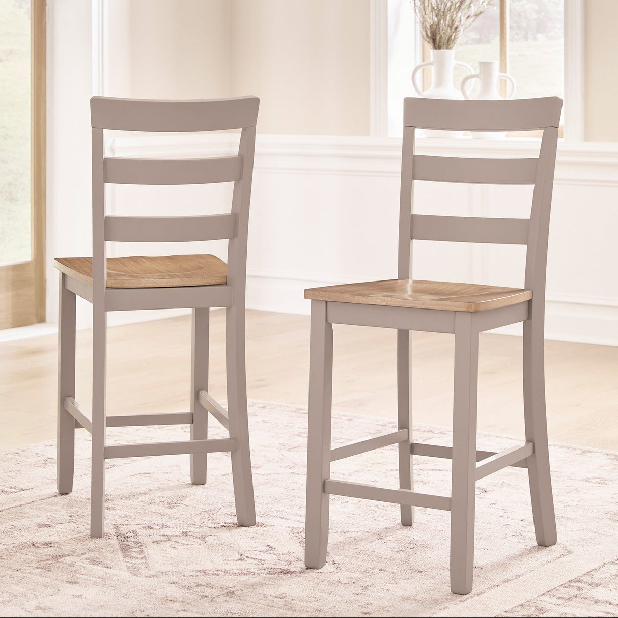 Two wooden bar stools with gray frames and wooden seats in a room with large windows.