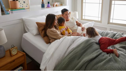 Family of four lying on a bed in a cozy bedroom.