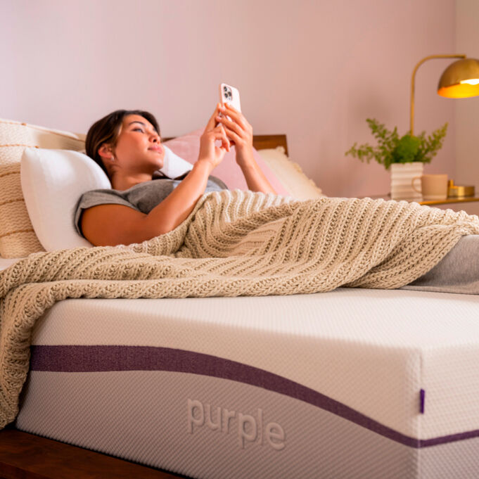 man laying on purple mattress on phone